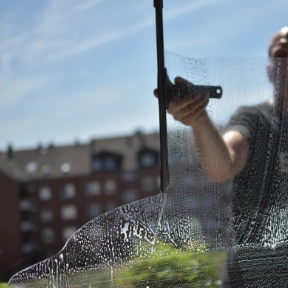 Fensterputzer reinigt Fensterscheibe mit Abzieher vor städtischem Hintergrund